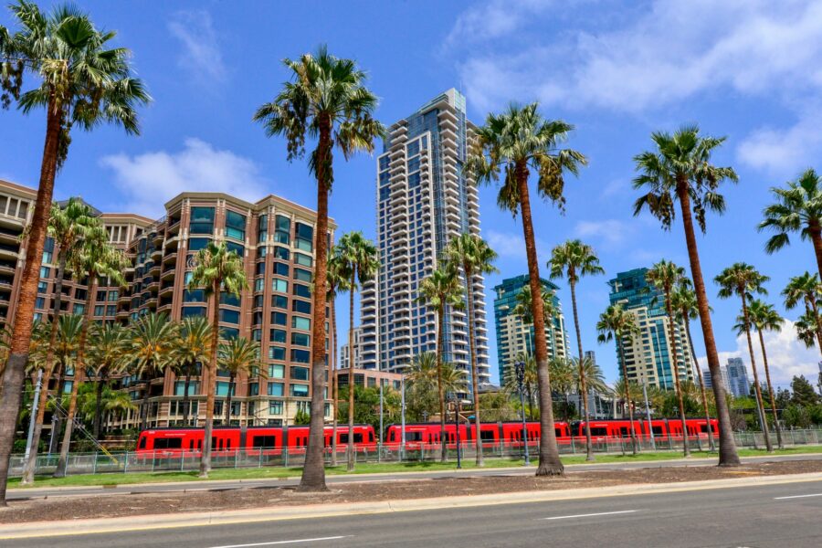 Red trolley passing tall buildings and palm trees in downtown San Diego. Photo by Pete Alexopoulos on Unsplash.